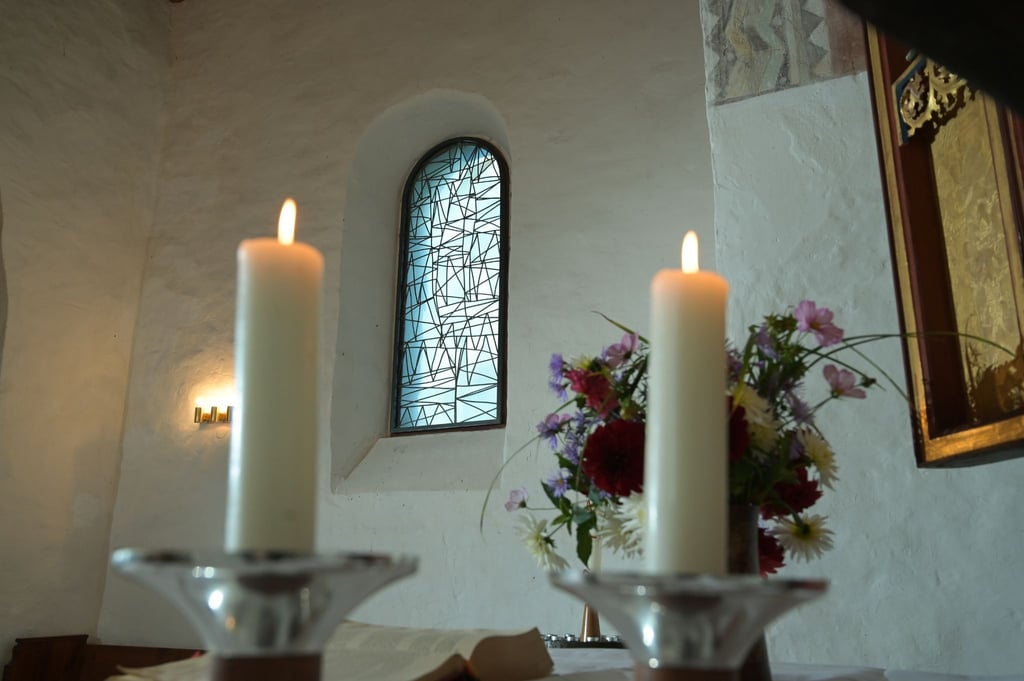 Kerzen brennen vor einem, der vom Künstler B. Muhr gestalteten modernen Kirchenfenster.