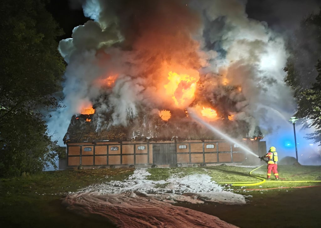 Feuerwehrleute löschen das Feuer in der mit Reet gedeckten Museumsscheune.