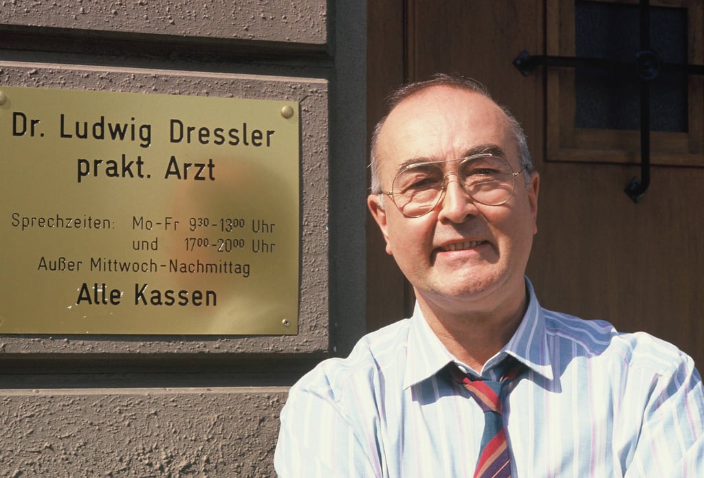 Schauspieler Ludwig Haas posiert in seiner Rolle als Dr. Ludwig Dressler vor dem Praxisschild in der Serie Lindenstrasse. Die Rolle verkörperte er knapp 35 Jahre.