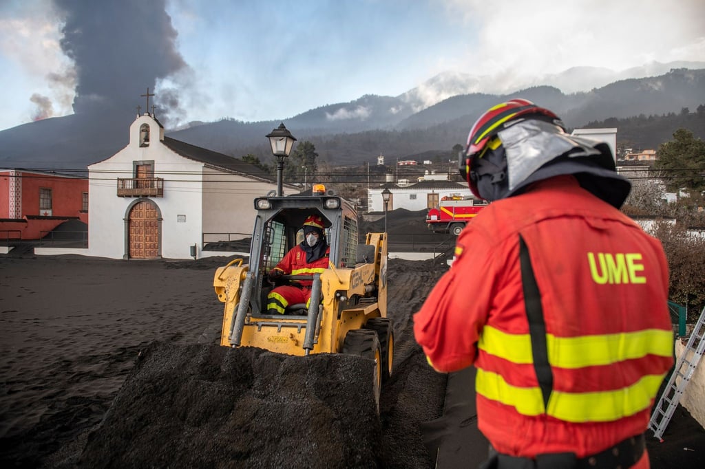 Einsatzkräfte des Militärs entfernen schwarze Asche vom Vulkan, der hinter der kleinen Kirche auf der Kanareninsel La Palma weiter Lava ausstößt.