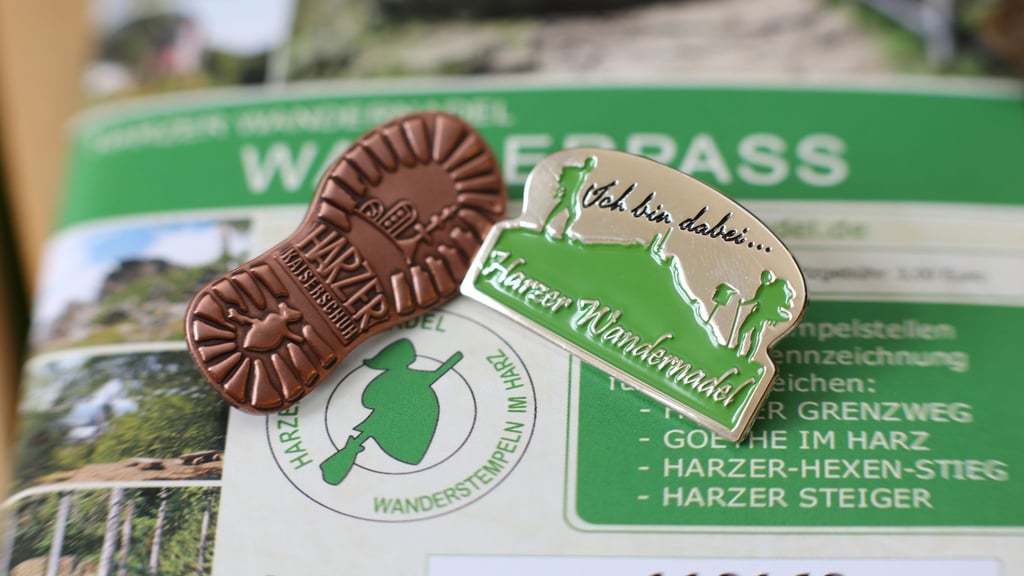 Abzeichen der Harzer Wandernadel liegen auf einem Wanderpass. Foto: Matthias Bein/