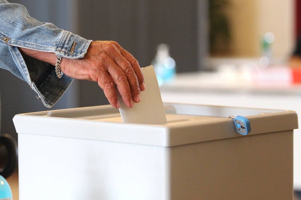 Ein Wahlzettel wird in eine Wahlurne gesteckt.