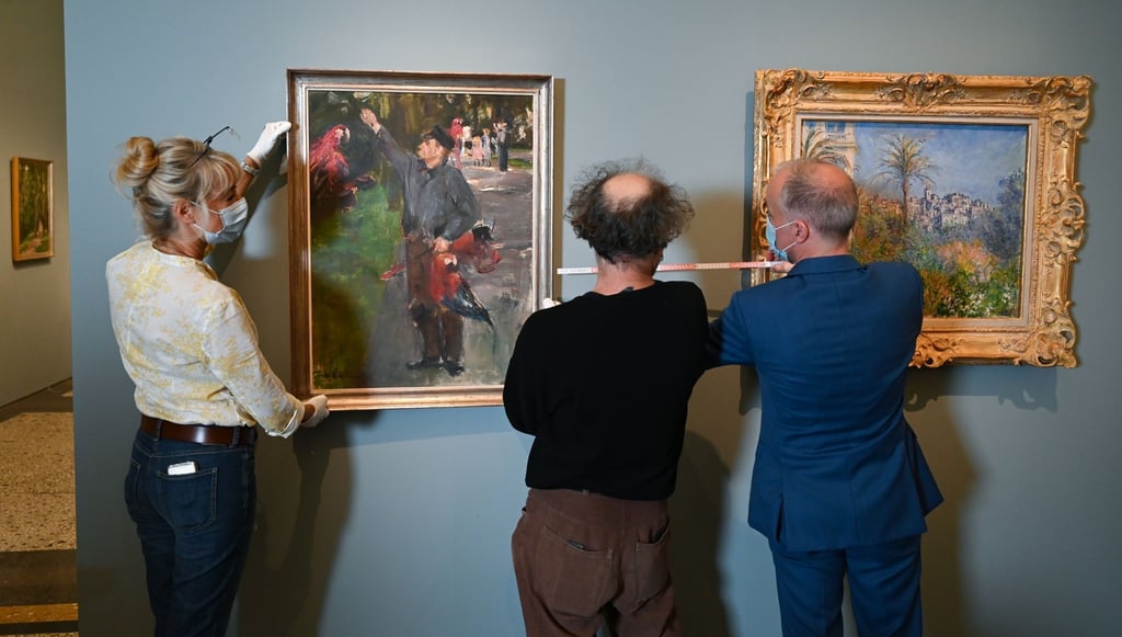Martin Faass (r), Direktor des Hessischen Landesmuseums Darmstadt, die Restauratorin Olivia Levental (l) und Depotverwalter Wolfgang Koch bereiten Liebermanns "Der Papageienmann (1900/01)"neben dem Gemälde "Villen in Bordighera (1884)" von Claude Monet für die Hängung vor.