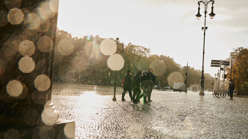 Menschen gehen in Sturm und Regen am Brandenburger Tor vorbei.