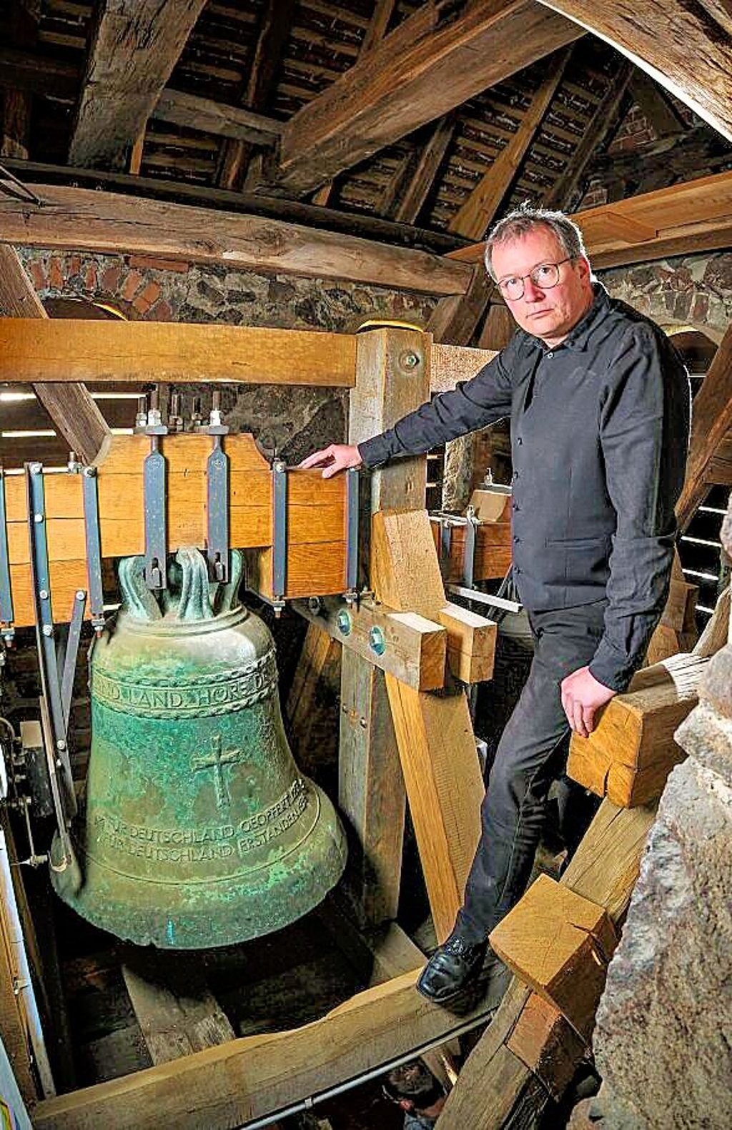 Pfarrer Albrecht Henning mit einer der Gossaer Glocken. Sie ist mit Nazi-Symbolik versehen.