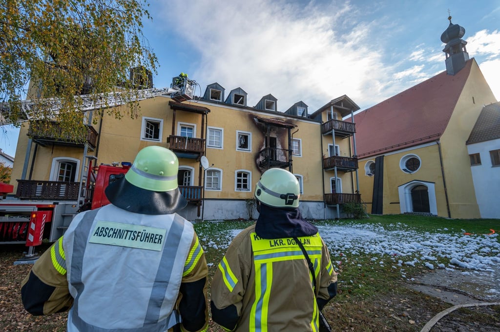 Feuerwehrmänner stehen vor einem ausgebrannten Mehrfamilienhaus.