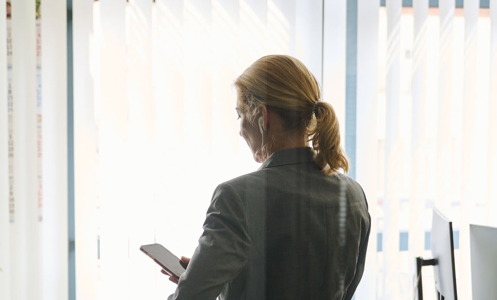 Eine Frau steht in einem Bürozimmer und hält ein Smartphone in der Hand. (Symbolbild)
