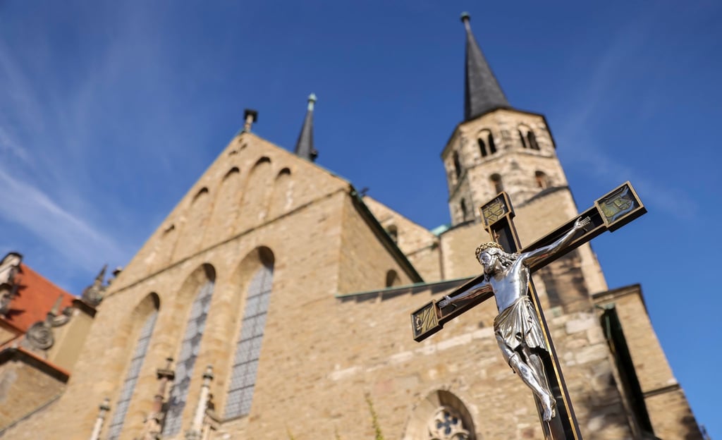 Ein Geistlicher hält ein Kreuz zur Glockenweihe vor dem Merseburger Dom.