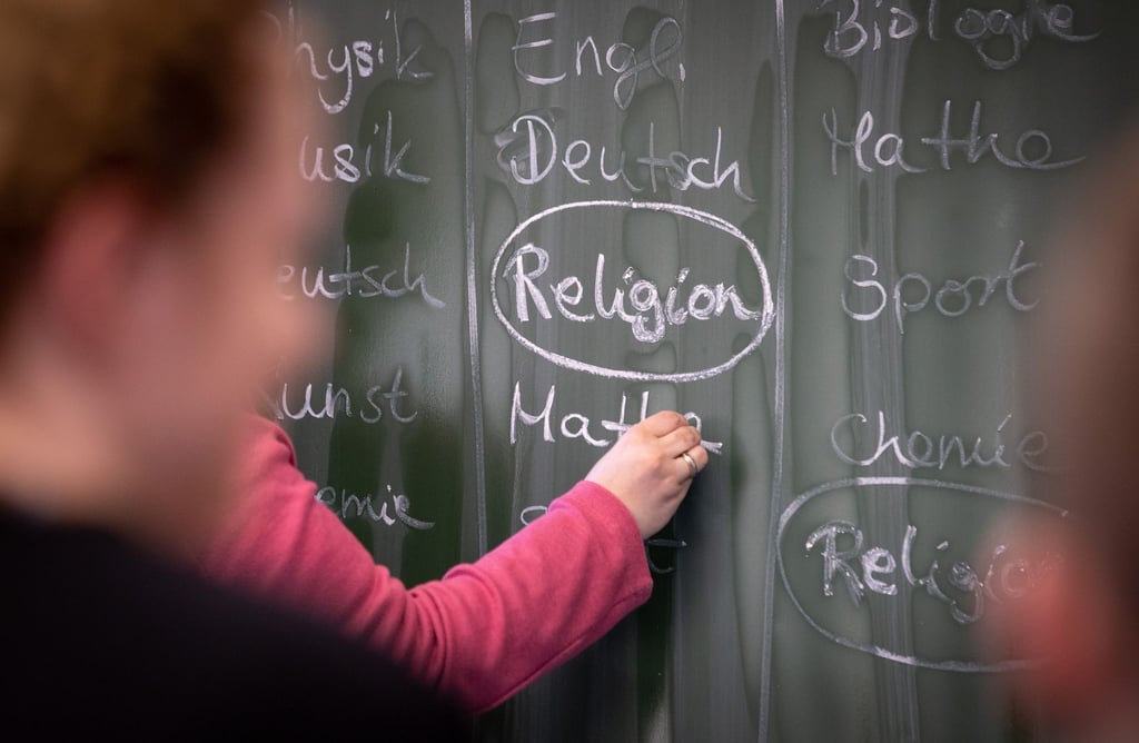 Eine Lehrerin schreibt mit Kreide einen Stundenplan mit Religionsunterricht an eine Tafel.