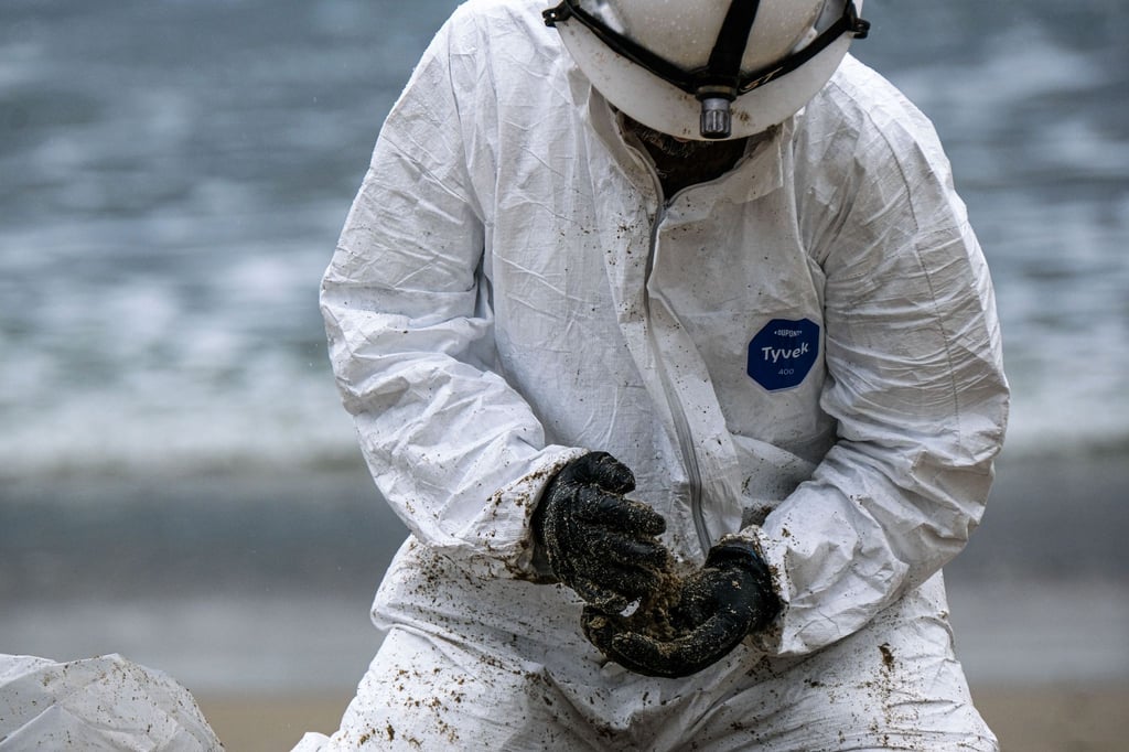 Ein Arbeiter in einem Schutzanzug säubert einen Strandabschnitt.