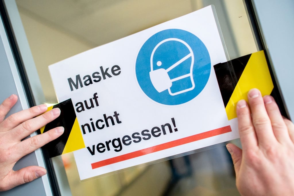 Ein Schild mit der Aufschrift „Maske auf nicht vergessen!“ an der Glasscheibe einer Schule.