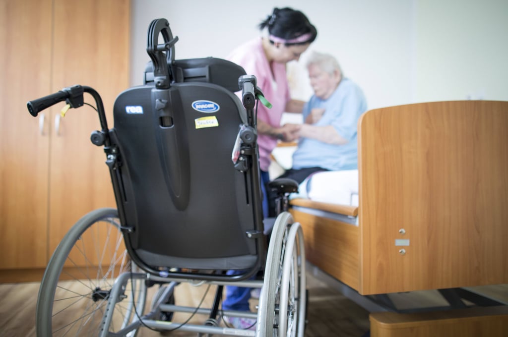 Eine Altenpflegerin hilft einer Bewohnerin in einem Altenpflegeheim aus dem Bett.