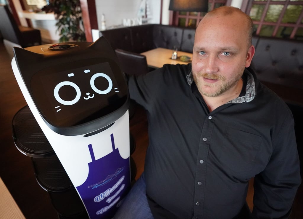 Gastwirt Tim Bornewasser in seinem Restaurant mit seiner digitalen „Mitarbeiterin“, dem Servierroboter „Bella“.