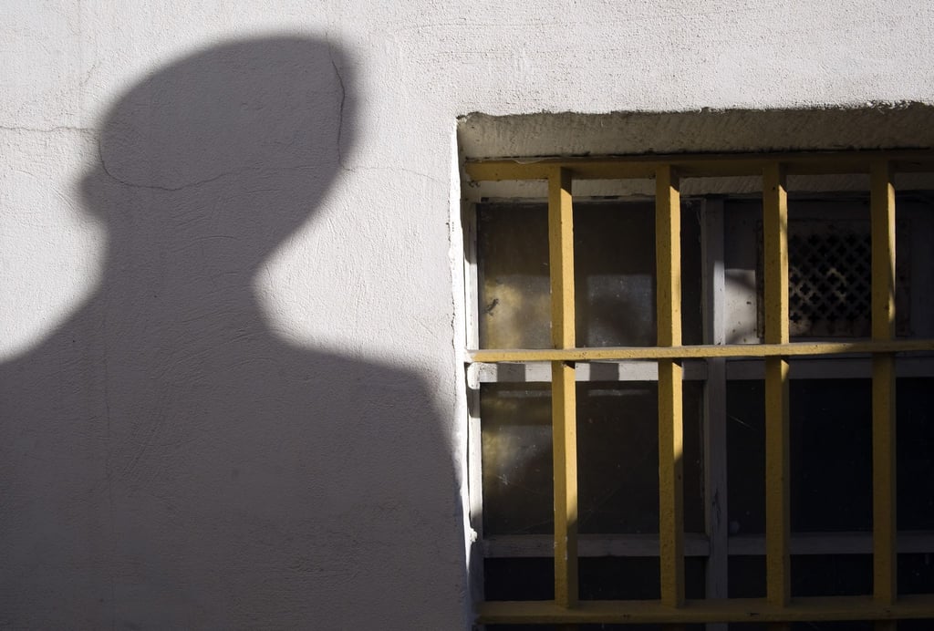 Der Schatten eines Mannes ist neben einem Gitterfenster zu sehen.