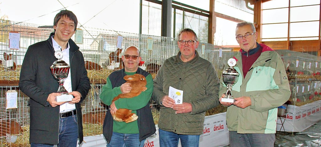 Schirmherr und Landrat Patrick Puhlmann (links) und Ortsbürgermeister Gerhard Borstell (rechts) präsentieren die von ihnen gestifteten Pokale. Vereinsvorsitzender Peter Komnick mit einem seiner roten Neuseeländer und Preisrichter Reiner Tietge aus Klötze freuen sich über die Unterstützung.