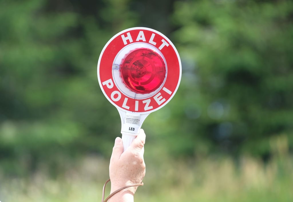 Eine Polizistin hält während einer Polizeikontrolle eine rote Winkerkelle in die Höhe.