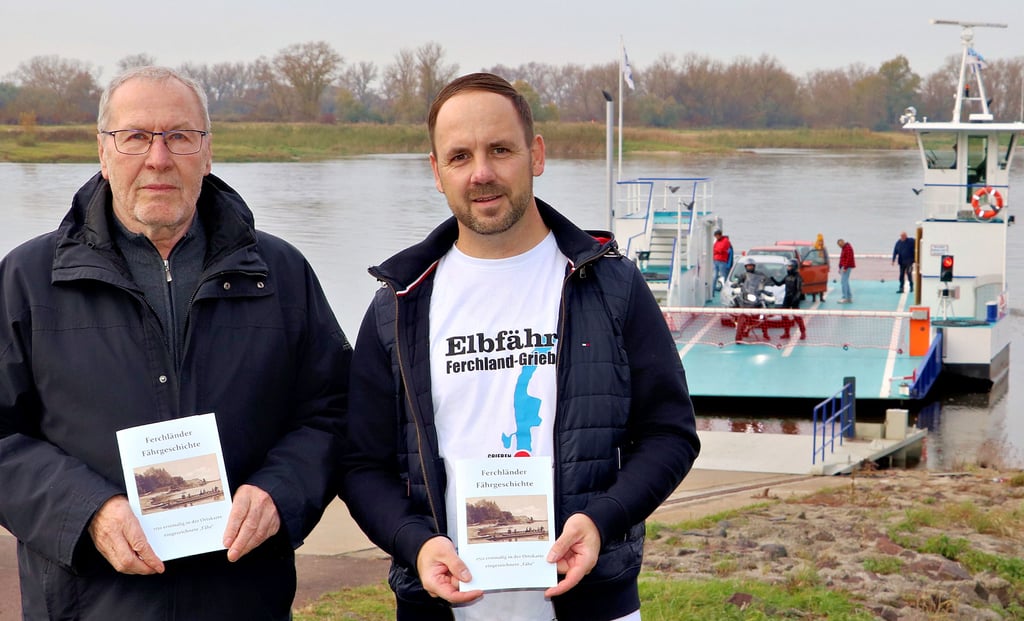 Ortschronist Horst Wedau und Heimatvereinsvorsitzender Daniel Richter (v. li.) mit der neuen Broschüre zur Ferchländer Fährgeschichte an der Fährstelle in Ferchland.