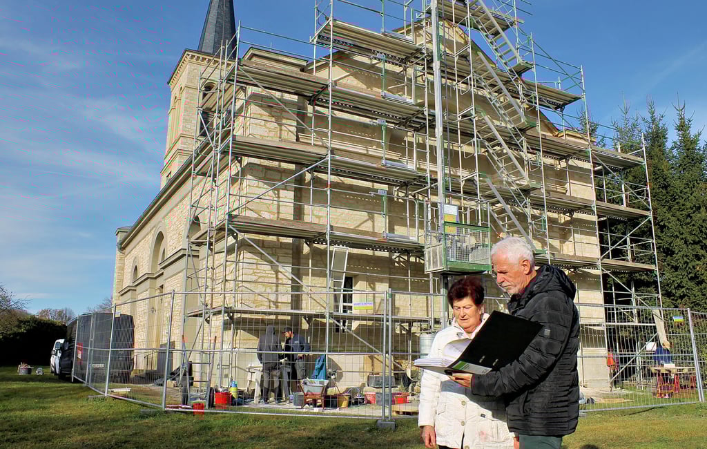 Helga Straub und Heudbers Ortsbürgermeister Hartmut Busch beim Blick in die Bauunterlagen. Im Hintergrund die Kirche mit der noch eingerüsteten Ostseite.