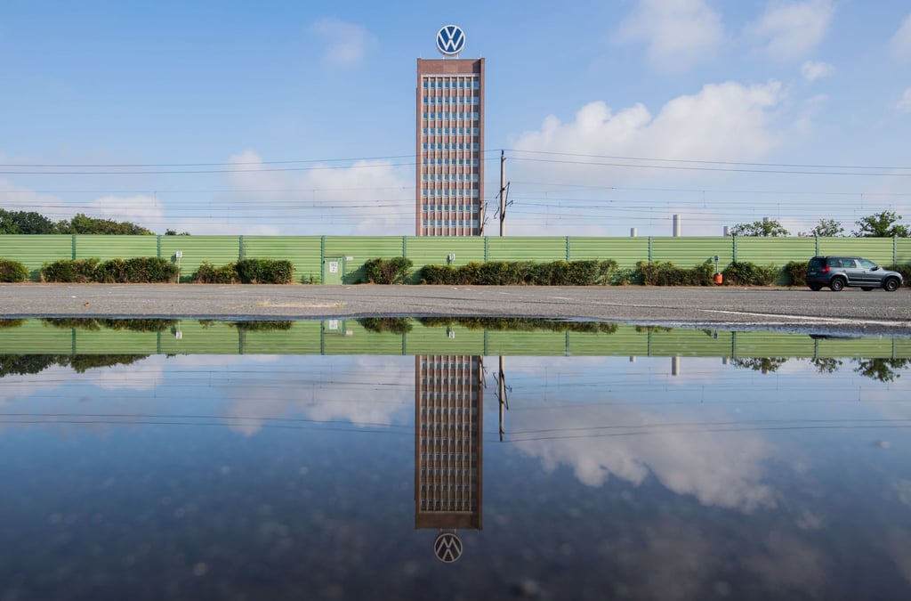 Das Markenhochhaus vom Volkswagen spiegelt sich in einer Pfütze auf einem Mitarbeiterparkplatz vor dem VW Werk Wolfsburg. (Archivbild)