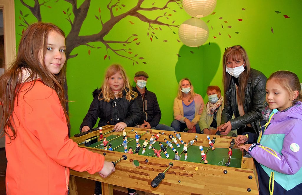 Sarah (v.l.), Jolina und Mia spielen Tischfußball, während Jugendbetreuerin Nicola Hirschel (r.) die Spielregeln erklärt. Zu den Gästen am Tag der offenen Tür des Calvörder Jugendclubs zählen Uwe Knake (hinten; v. l.), Sandra Nisar und Heidemarie Schweickert.