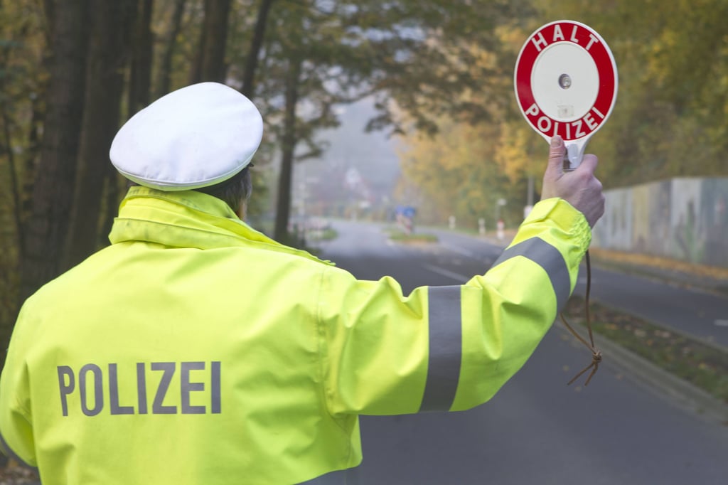 Ein Polizist hebt am Straßenrand eine Anhaltekelle.