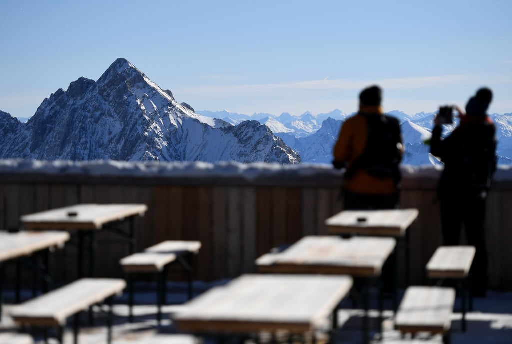 Zwei Besucher fotografieren von der Zugspitze aus das Panorama des Wettersteingebirges. Nach gut eineinhalbjähriger Pause wegen Corona sollen dort wieder Lifte laufen und Skifahrer ihre Schwünge ziehen.