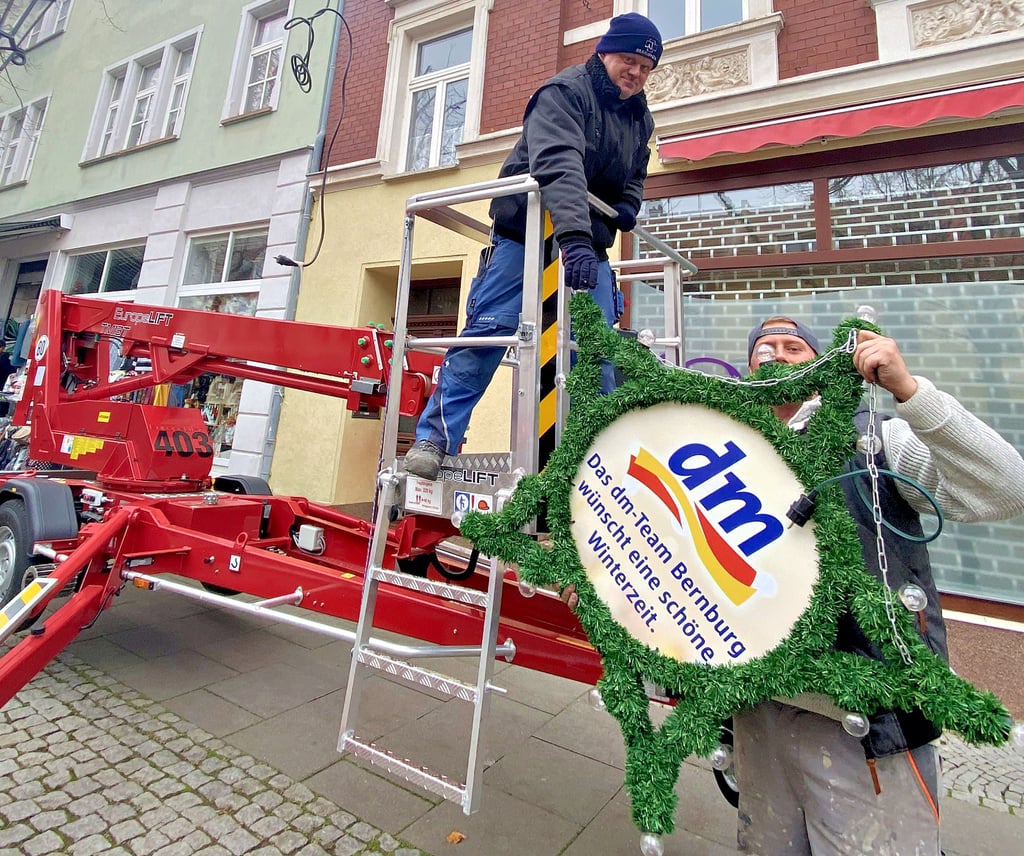 René König (von links) und René Liebner, Mitarbeiter der Elektrotechnik Eckert & Wiethake GmbH, bringen die Weihnachtsbeleuchtung in der Bernburger Innenstadt an.