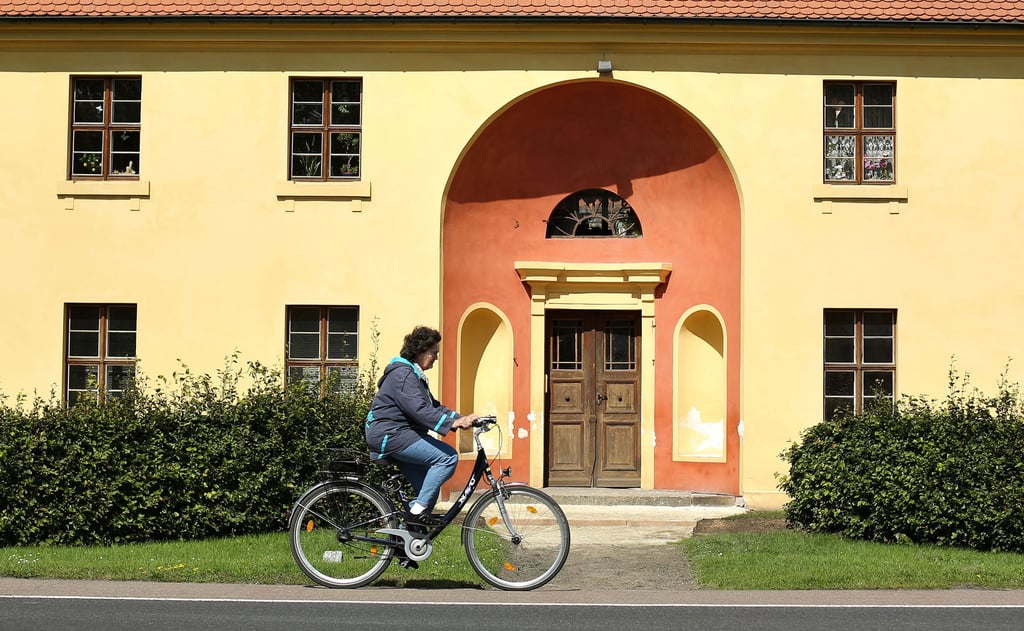 Eine Frau fährt mit dem Fahrrad bei Sonnenschein vor der Orangerie des Schlosses Oranienbaum entlang.