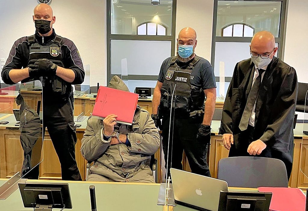 Der Angeklagte versteckt sich hinter einem roten Aktenordner, während er auf seinen Prozess wartet.