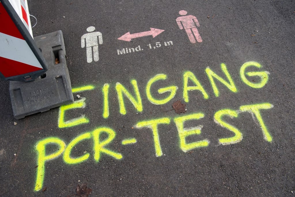 Die Worte „Eingang PCR-Test“ sind mit gelber Farbe vor einem Corona-Testzentrum auf die Straße gemalt worden.