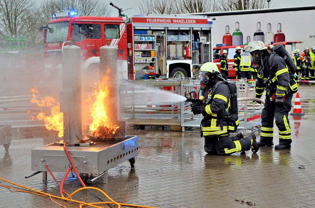 Eine Simulationsanlage zeigt den Brand einer Gasflsche, der von zwei Wehrleuten mit Atemschutzmasken professionell gelöscht wird. Dabei wird Wasser eingesetzt.