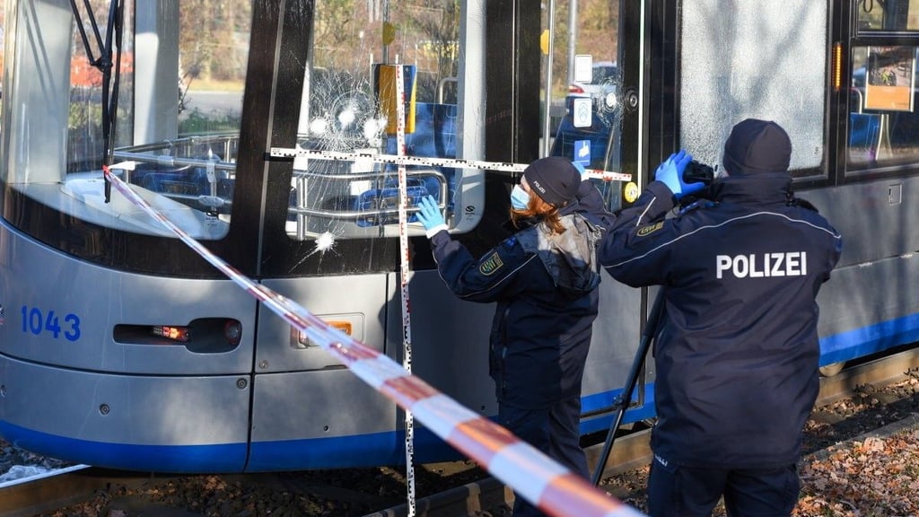 Polizisten begutachten eine zersplitterte Scheibe einer Straßenbahn. Ein Mann hatte Steine aus dem Gleisbett auf eine fahrende Straßenbahn in Leipzig geworfen und mehrere Scheiben zerstört.
