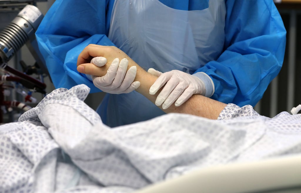 Im Infektionszimmer für Covid-19-Patienten hält die Mitarbeiterin einer Intensivstation die Hand eines Patienten.
