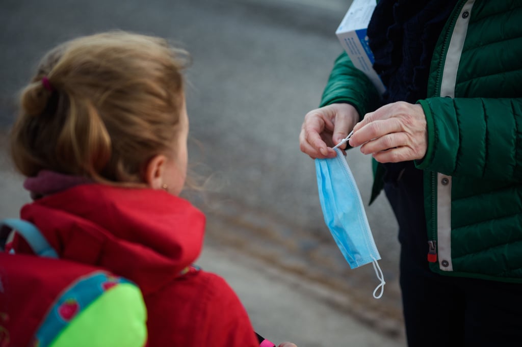 Eine Lehrerin kürzt einen Mund-Nasen-Schutz für eine Schülerin vor dem Unterricht in einer Grundschule.
