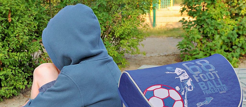 Ein Kind sitzt mit seinem Ranzen auf einer Tischtennisplatte. Durch Corona hat schulvermeidendes Verhalten zugenommen.
