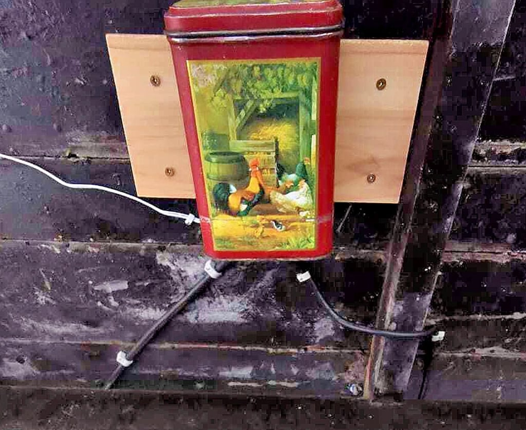 Eine ausrangierte Kaffeebüchse mit Hühnchen und Hähnchen bietet dem Elektro-Netzteil für die LED-Lampenkette Schutz.