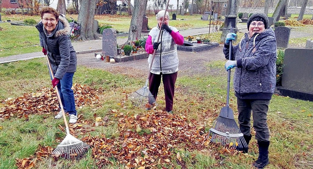 Christa Merker (v.l.), Gudrun Homann und Helga Märtens harken beim Arbeitseinsatz auf dem Friedhof die Blätter zusammen.