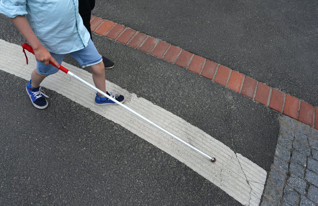 Ein blindes Kind überquert die Straße mithilfe eines Gehstocks und wird dabei begleitet. Eine Mutter aus Salzwedel ringt für ihre blinde Tochter bei Ämtern um Unterstützung, denn ihr Kind benötigt jede Hilfe, die es kriegen kann.