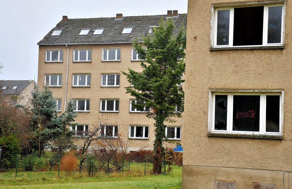 Blick vom Gehweg an der Schulstraße (Spielplatz Kinder-Eltern-Zentrum Seeperle) in Richtung der Straße Dessauer Worth. Von dort sind drei der vier verfallenen Wohnblöcke, in denen sich ingesamt 104 Wohneinheiten befinden, zu sehen.