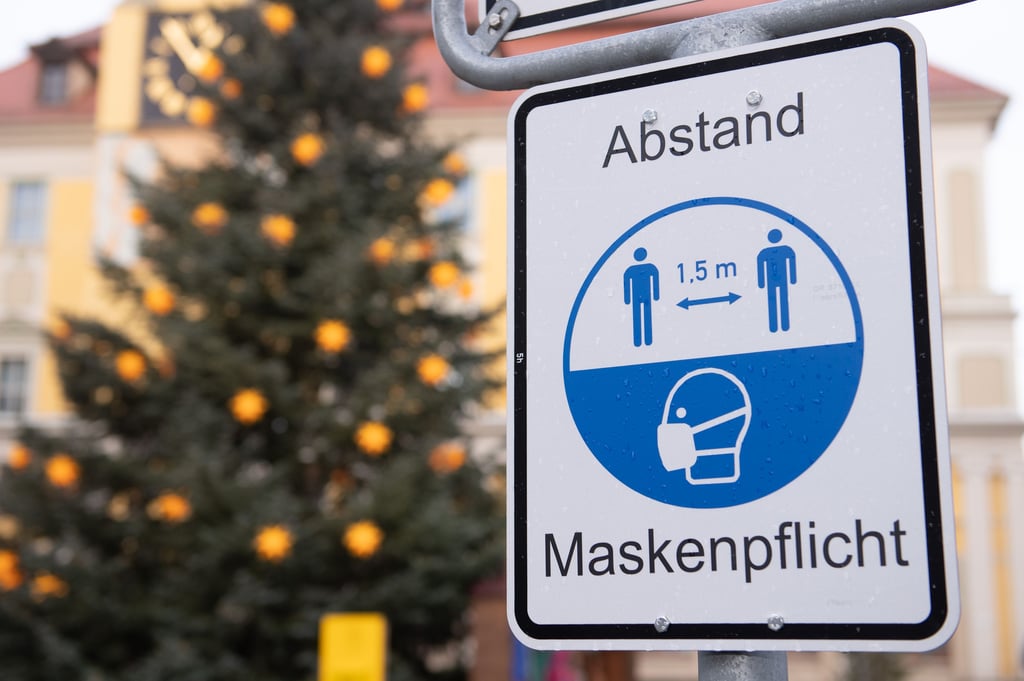 Ein Hinweisschild für die Maskenpflicht und den Abstand hängt an einem Marktplatz vor einem Weihnachtsbaum.