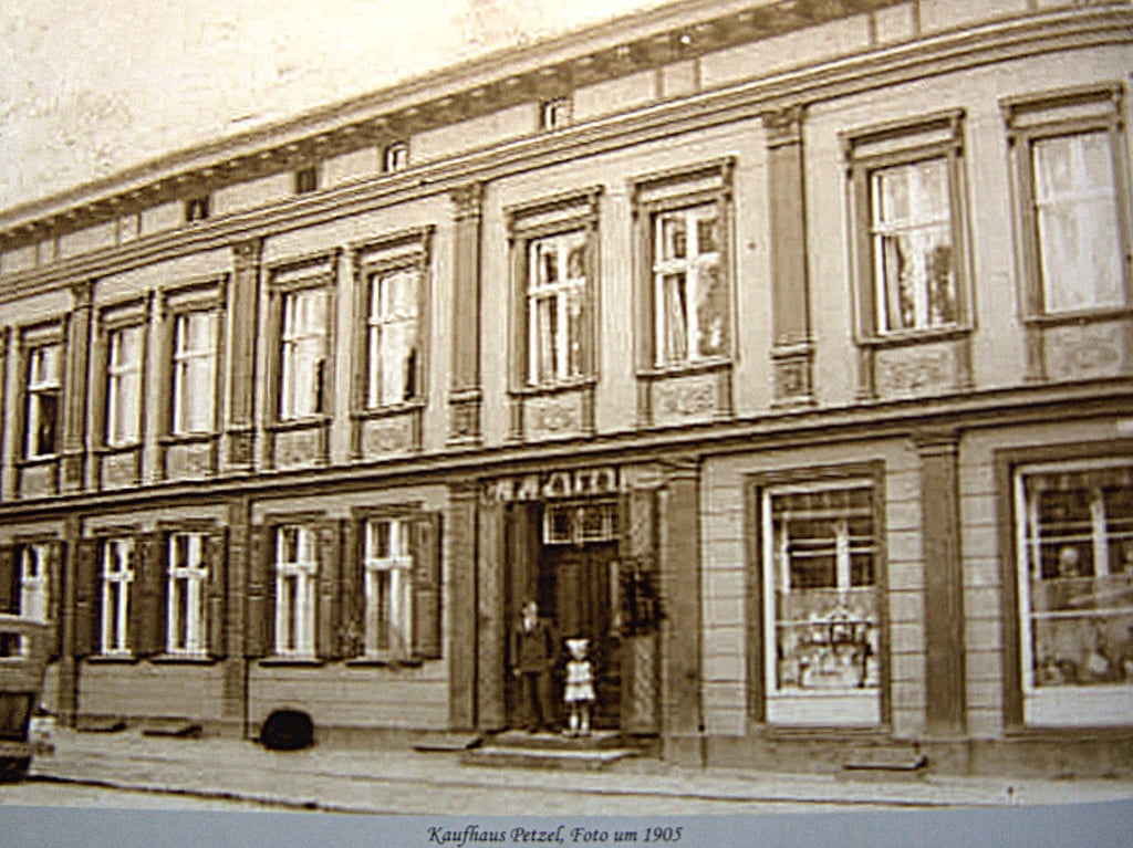 So sah das Geschäftshaus Petzel 1905 an der Ecke Karl-Liebknecht-Straße – Friedrich-Naumann-Straße aus. Es wurde 2002 abgerissen und ein Spielplatz errichtet. Der Ort trägt heute den Namen „Behrens-Petzel-Platz“.