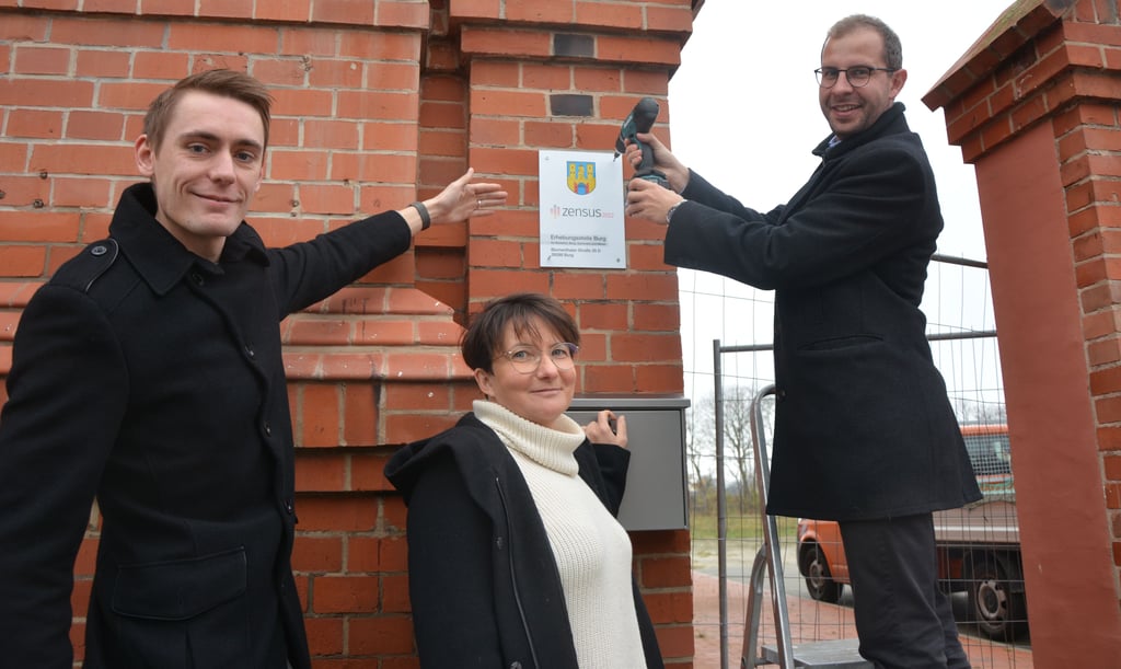 Am Verwaltungsgebäude des ehemaligen Schlachthofes an der Blumenthaler Straße in Burg schraubt Bürgermeister Philipp Stark die letzte Schraube des Zensus-Hinweisschildes in die Mauer. René Teßmann und Doreen Wichmann sind die ersten Mieter im denkmalgeschützten Haus.