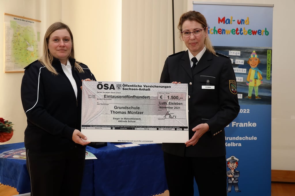 Die amtierende Revierleiterin Annerose Rost (li.) und Polizeisprecherin Steffi Schwan mit dem Scheck, den die Eisleber Grundschule "Thomas Müntzer" im Rahmen des Malwettbewerbs gewonnen hat.