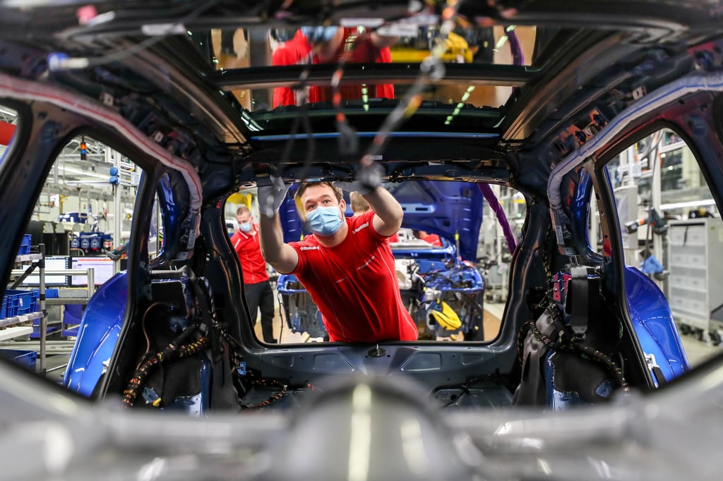 Ein Mitarbeiter von Porsche arbeitet mit Mundschutz in der Montage an einem Macan.