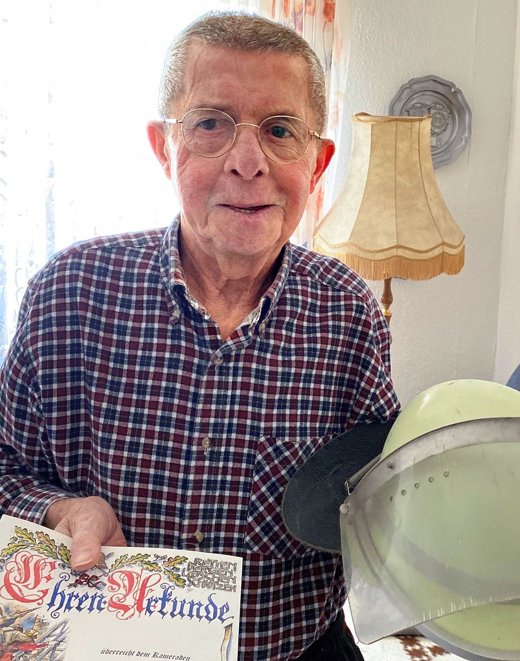 Achim Pätz mit seinem alten Einsatzhelm und der Ehrenurkunde für 70 Jahre Feuerwehr.