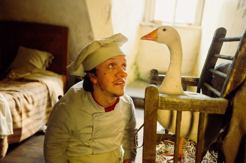 Inmitten seiner ärmlichen Kammer kniet Zwerg Nase (Mick Mehnert) vor einem Holzkäfig, aus dem die Gans Mimi hinausschaut.