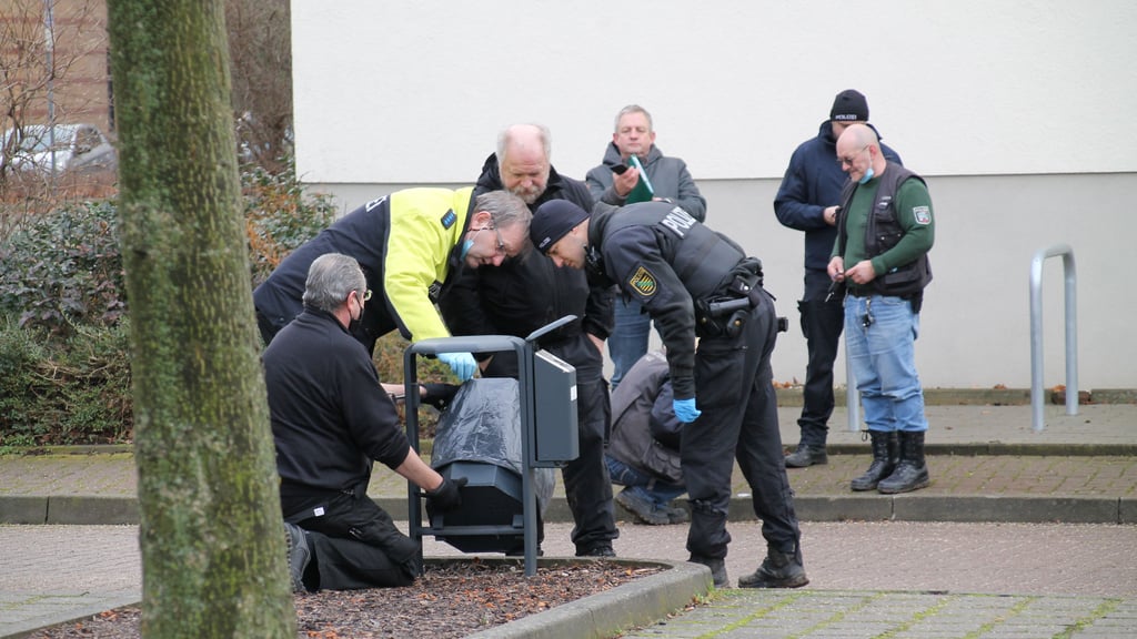 Polizisten und Kriminaltechniker untersuchen einen Papierkorb.