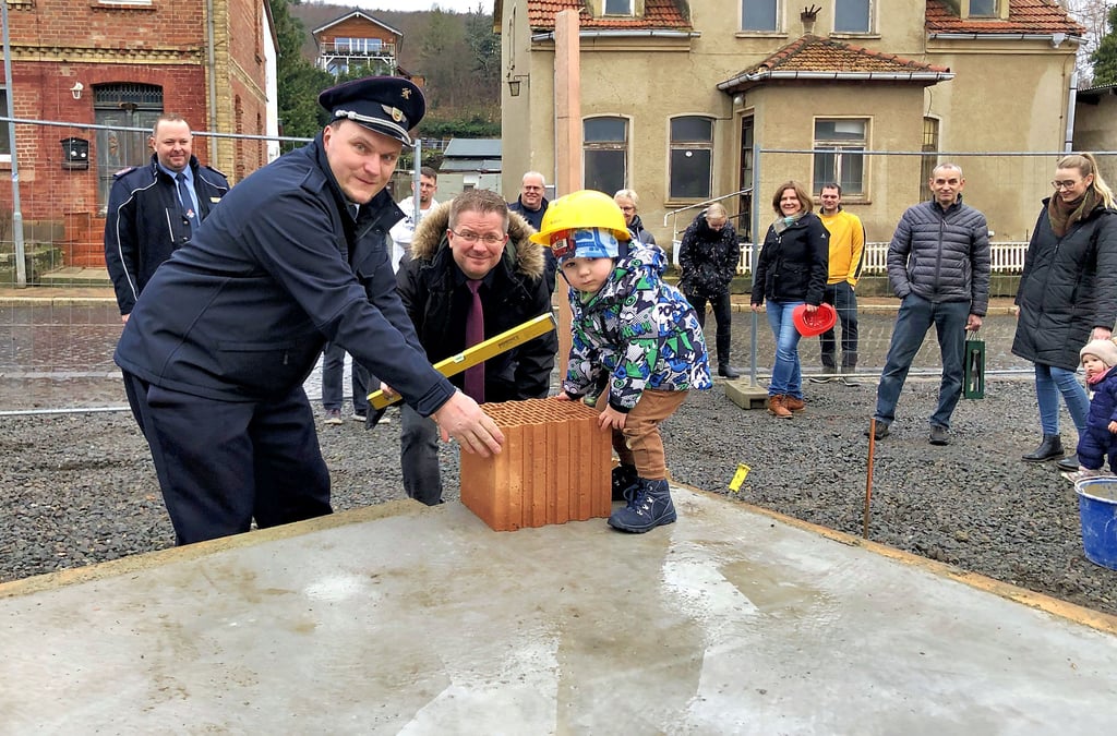 Im Beisein vieler Interessierter setzen Ortswehrleiter Patrick Müller, Thales Bürgermeister Maik Zedschack und der zweijährige Tim bei der Grundsteinlegung den ersten Stein auf die Bodenplatte.