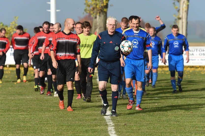 Schiedsrichter Siegfried Zille führt in Baumersroda die Teams aufs Feld.