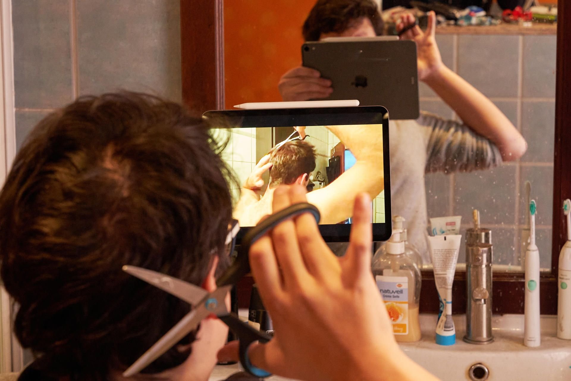 Ein junger Mann schneidet sich nach Anleitung eines Online-Tutorials selber die Haare. Für Kunden und Friseure ist es eine Erlösung: Seit dem 01.03.2021 haben die Salons nach ihrer Corona-Zwangspause wieder geöffnet.